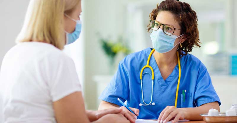 Patient talking to medical professional, wearing masks Patient talking to medical professional, wearing masks